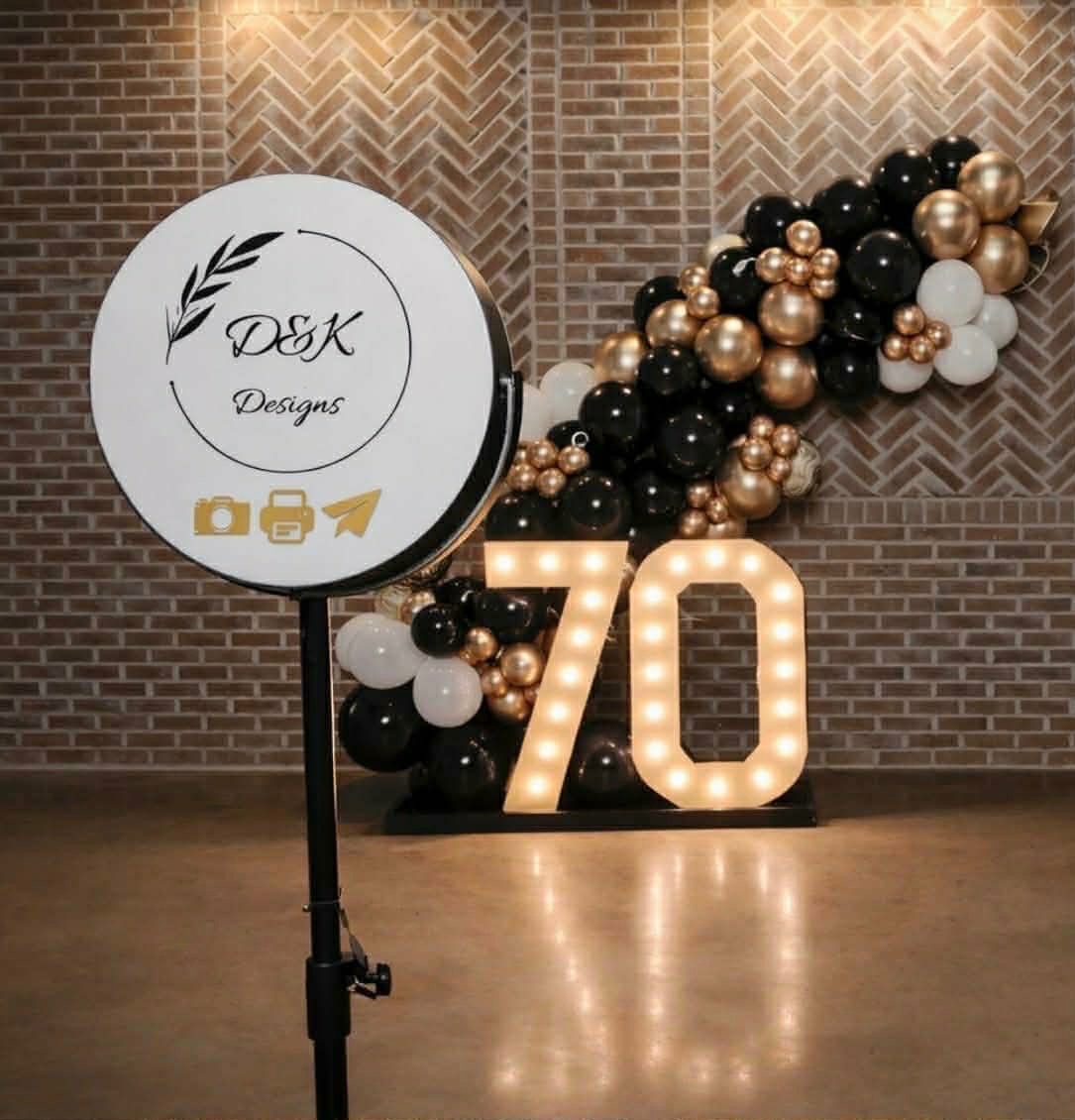 Basic photo booth setup with DK217Designs ring light, black and gold balloon garland, and light-up 70 marquee